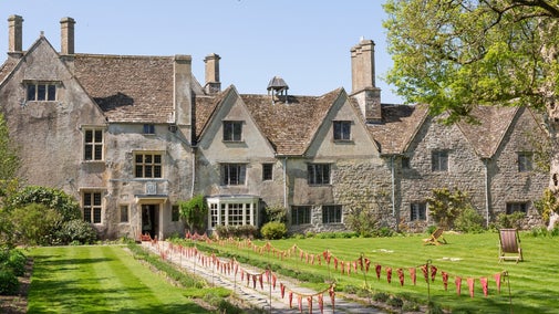 A wide photo of Avebury Manor taken from the end of the Lavender Walk on the East Lawn, flanked by green trees and a bright blue sky.